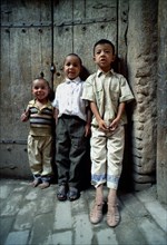 CHINA, Xinjiang, Kashgar, Three young boys standing against a wooden door on a cobbled street