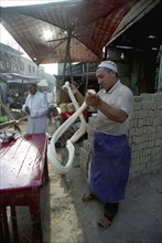 CHINA, Xinjiang, Kashgar, Man spinning dough at a street side stall