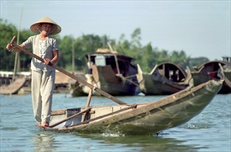 VIETNAM, Central, Hue, Local transport woman standing on the edge of her canoe rowing with a single