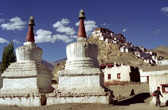 INDIA, Ladakh, Tikse, Tikse Gompa. Twin red and white stupas with hilltop architecture beyond