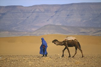 MOROCCO, Transport, Touareg man leading camel through desert.