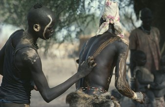 SUDAN, Body Decoration, Dinka tribesman painting the back of another with dung ash.