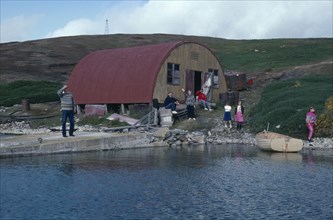 FALKLAND ISLANDS, West Point Island, View across water towards loading jetty with a family near