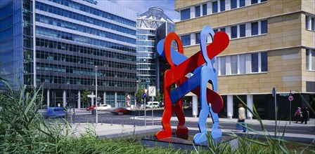 GERMANY, Berlin, Red and blue sculpture by Keith Haring entitled Boxers with city road and