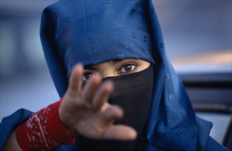 MOROCCO, Marrakech, Portrait of young veiled woman reaching towards camera possibly to stop