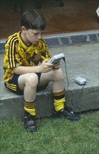 CHILDREN, Play, Computer Games, Young boy in a football kit playing a Nintendo Gameboy