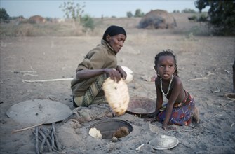 ETHIOPIA, Danakil Depression, Afar woman and child cooking in oven in ground.