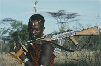 UGANDA,   , Karamoja, "Portrait of Karamojong warrior with ostrich feather in hair holding gun and