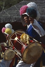 SOUTH KOREA, Arts, Dance, Farmers Dance.  Young man wearing paper flowered hat and playing drum.