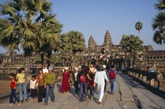 CAMBODIA, Siem Reap Province, Angkor Wat, Tourists on tree lined stone causeway leading to temple