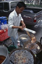 THAILAND, South, Bangkok, Thanon Silom male vendor at his stall on the pavement deep frying fish in