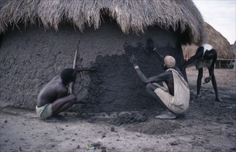 SUDAN, People, Shilluk men using mud to plaster the wall of a hut.