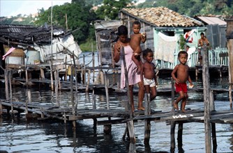 BRAZIL, Bahia, Salvador da Bahia, Young woman with three children crossing wooden bridge over water
