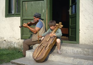 ROMANIA, Transylvania, Gimes Village, "Man and child playing violin and a gardon, a cello like