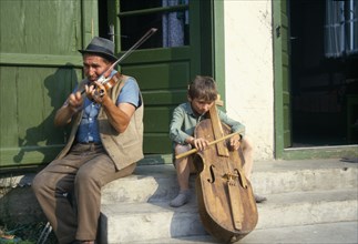 ROMANIA, Transylvania, Gimes Village, "Man and child playing violin and a gardon, a cello like