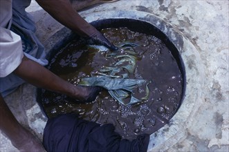 NIGERIA, Kano, Cropped view of worker and indigo dye pit.  To achieve a  dark colour requires