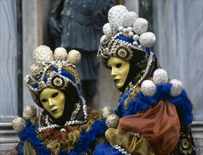 ITALY, Veneto, Venice, Venice Carnevale. Two figures dressed in elaborate costumes and gold masks