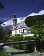 GERMANY, Bavaria, Ramsau, View over river and wooden bridge towards Ramsau Church and wooded