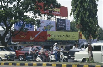 INDIA, Karnataka, Bangalore, Street scene with cars and mopeds passing advertising hoardings.