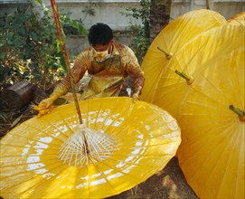 THAILAND, Chiang Mai Province, Bo Sang Village, Man spinning cotton umbrella as he applies colour