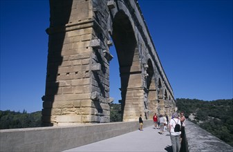 FRANCE, Languedoc Roussillon , Gard, Pont du Gard Roman aqueduct.  Tourists on bridge beside arches