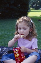 ENGLAND, West Sussex, Chichester, The Bishops Palace Gardens.  Girl aged three eating potato crisp