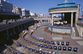 20059185 ENGLAND East Sussex Eastbourne View towards the Promenade Band Stand with a brass band performing on a sunny day and spectators watching from deckchairs layed out in a semi-circle.