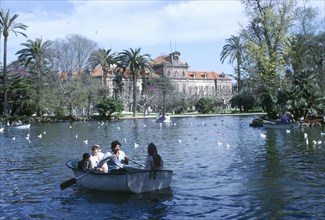 SPAIN, Catalonia, Barcelona, Family in rowing boat on lake in front of the Catalan Parliament