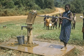 GHANA, Euchi, Young girl using village hand pump to draw water.
