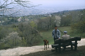HUNGARY, Budapest, Dog walkers in conversation in park above city.