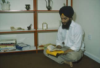 ENGLAND, Religion, Skihism, Sikh man sitting on the floor of his home reading Gutka an abbreviated