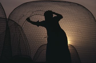 UAE, Industry, Fishing, Fisherman mending net silhouetted against sunset sky.