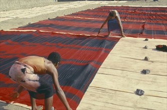YEMEN, Al Hudaydah, Laying red and black striped cloth out to dry.
