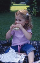 ENGLAND, West Sussex, Chichester, The Bishops Palace Gardens.  Girl aged three eating brown bread