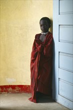 TANZANIA, Ngorongoro, Masai child standing between yellow wall and blue door.  The Masai have been
