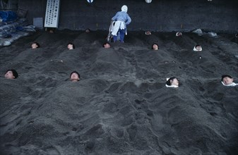JAPAN, Kyushu, Ibusuki, Hot Sand Bath. People submerged in sand with their heads pocking out above
