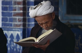 CHINA, Xinjiang Province, Religion, Iman Holyman with head down reading in mosque.
