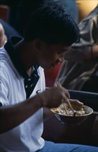 THAILAND, South, Bangkok, Damnoen Saduak Floating Market man sitting in a canoe eating noodles