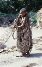 CONGO, The Ituri Forest, Pygmy boy sorting fishing nets on sand for hunting trip.