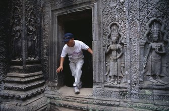 CAMBODIA, Siem Reap Province, Angkor, Ta Prohm.  Visitor climbing through doorway of twelth century