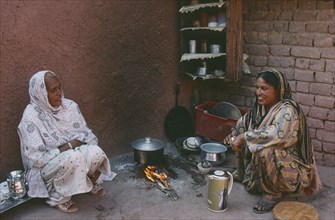 PAKISTAN, Food, Two women cooking over open wood fire in corner of building.