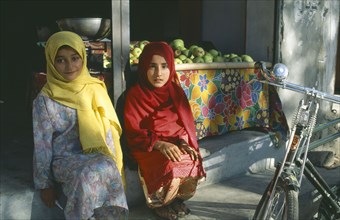 PAKISTAN, Northern Areas, Gilgit, Two young girls sitting on step beside roadside fruit stall.