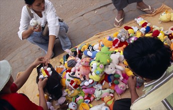CAMBODIA, Siem Reap, Woman buying from a pavement vendor with a display of soft toys for sale