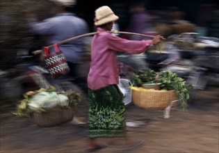 CAMBODIA, Siem Reap, Woman carrying fresh produce in two baskets balanced on a pole over her