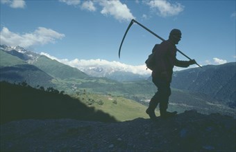 GEORGIA, Caucasus Mountains, Silhouetted figure of man carrying scythe with mountain backdrop.