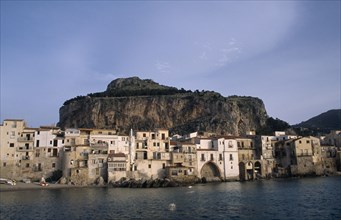 ITALY, Sicily, Cefalu, Town houses on edge of water with huge rock behind once the site of a Temple