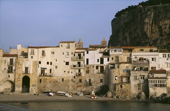 ITALY, Sicily, Cefalu, Town houses on edge of water with huge rock behind once the site of a Temple