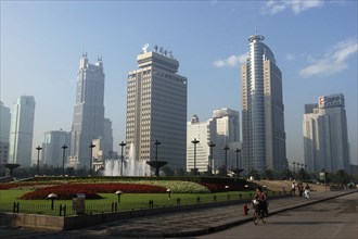 CHINA, Shanghai, Modern city skyline with flowerbeds and fountain in the foreground with passing