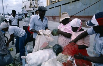 WEST INDIES, Nevis, People unloading sacks of goods at port with cargo ship in background.