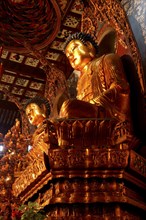 CHINA, Shanghai, Jade Buddha Temple. Seated golden Buddha statues in an elaborate surrounding